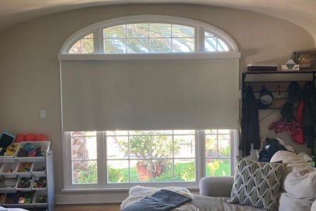 Custom roller shade partially open on a large arched living room window, showing natural light and modern design in an Oakland home.